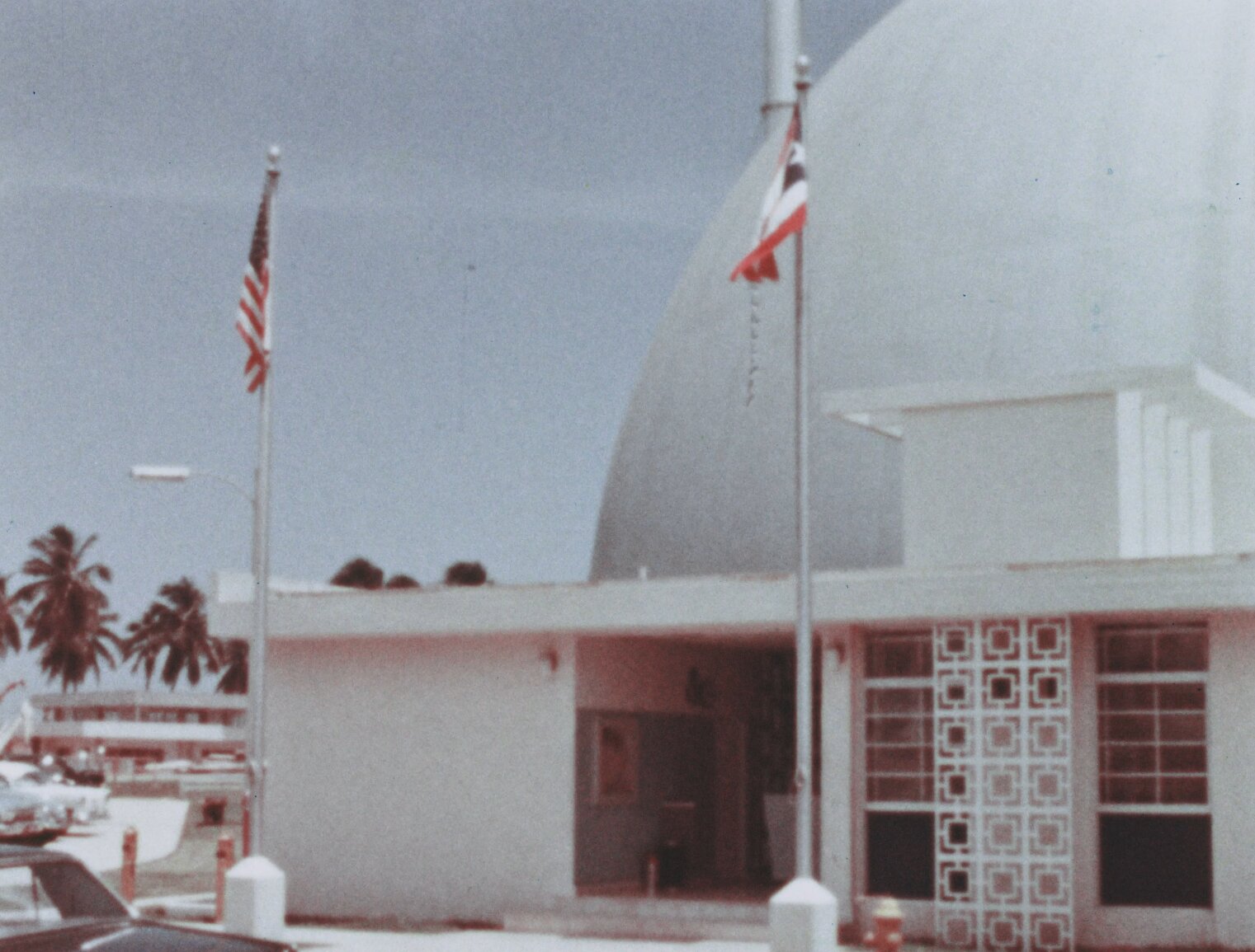 The front door to the bonus building showing an american and Puerto Rican flag side by side. Dome and palm trees in background.