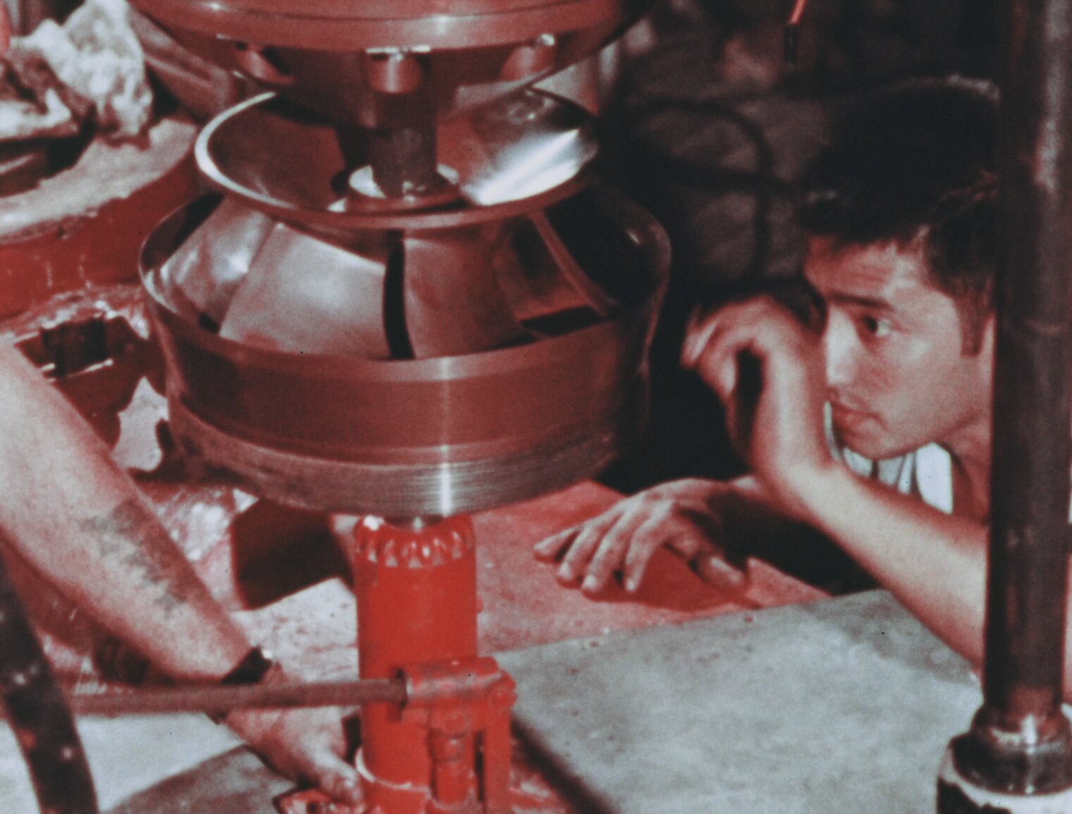 Man looks at broken nuclear recirculation pump while trying to fix it. It is jacked up on a red jack.