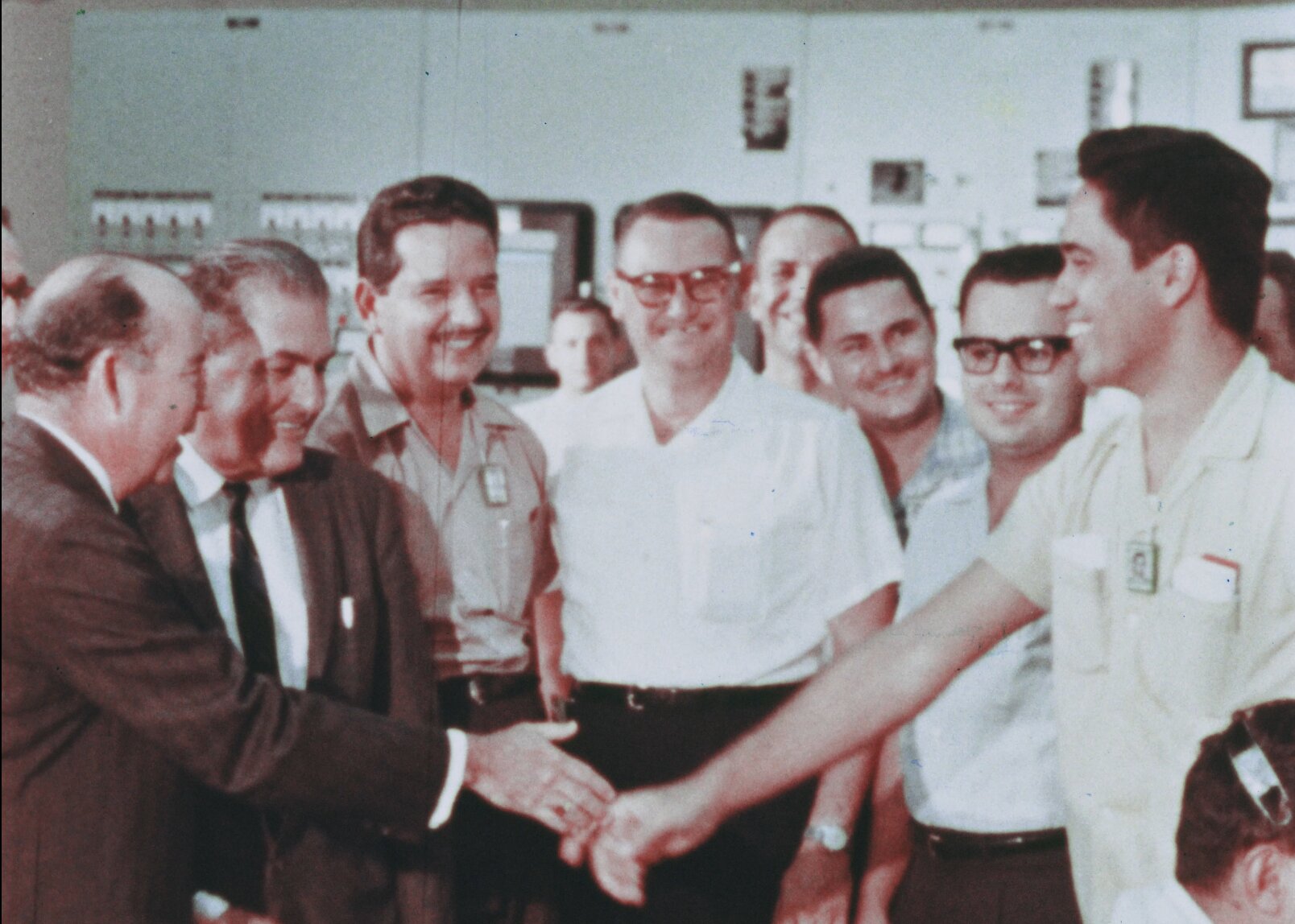 11 smiling men shaking hands in the control room of bonus after achieving initial criticality.