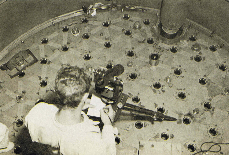 Surveyor with survey tool pointed down at metal plate filled with holes