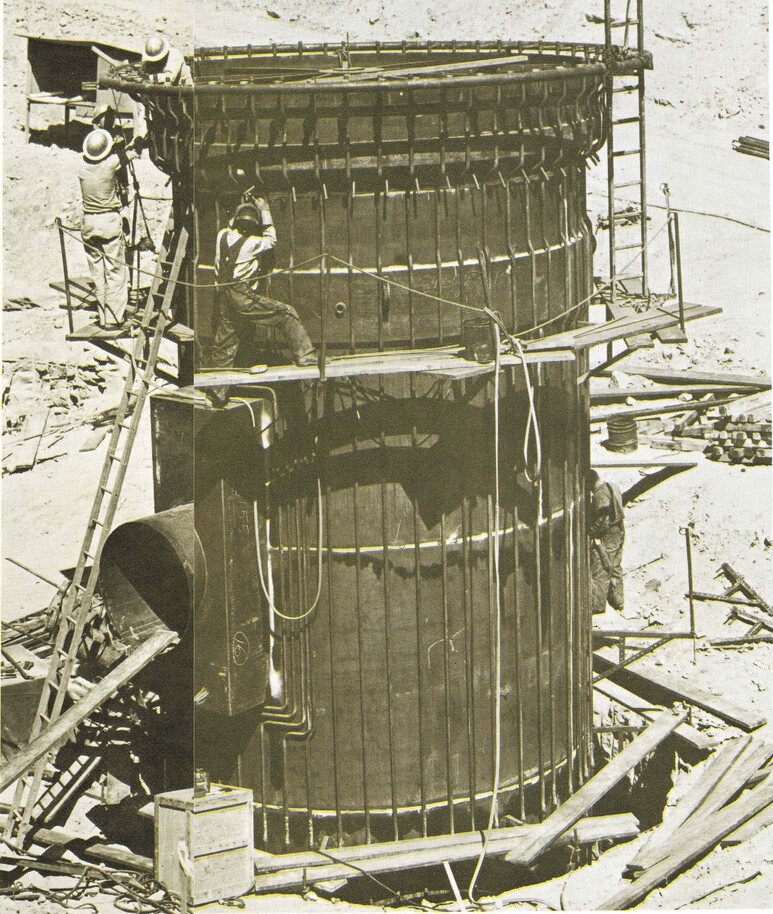 A large cylinder with workers hanging off it and with coolant tubes all around it